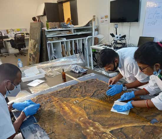Participant-conservators at KIAC setting and flattening a waterlogged oil painting, using a strategy devised by course mentor Sanjay Dhar