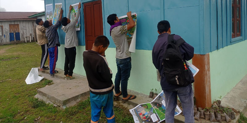 WATSAN committee members pasting SBCC posters in communal spaces in the village