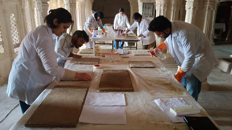 Participants executing tracing for their individual designs on mud plaster