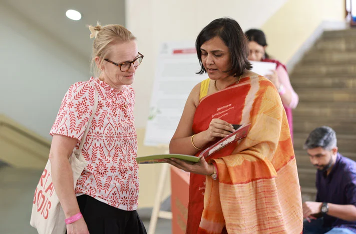 Maulshree Kalothia from Tata Trusts interacts with a guest at the Parag Collab Art Wall, sharing insights into the children's artworks and the stories behind them.